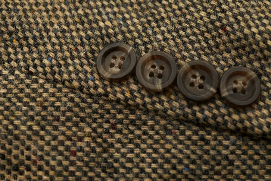 Close view of a woven tweed cloth in browns and olive with horn buttons