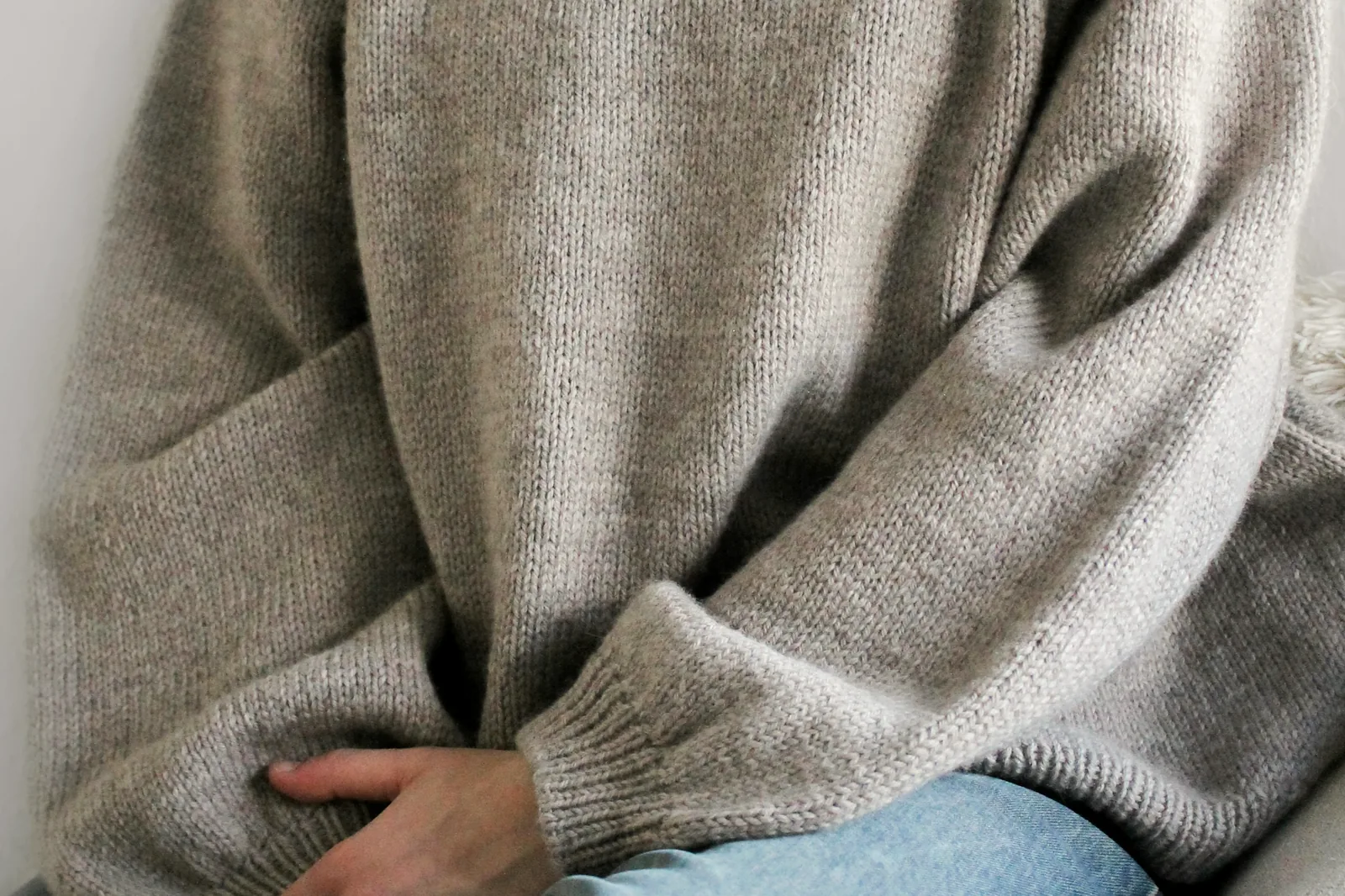 A plain grey knitted sweater worn, seen from the side